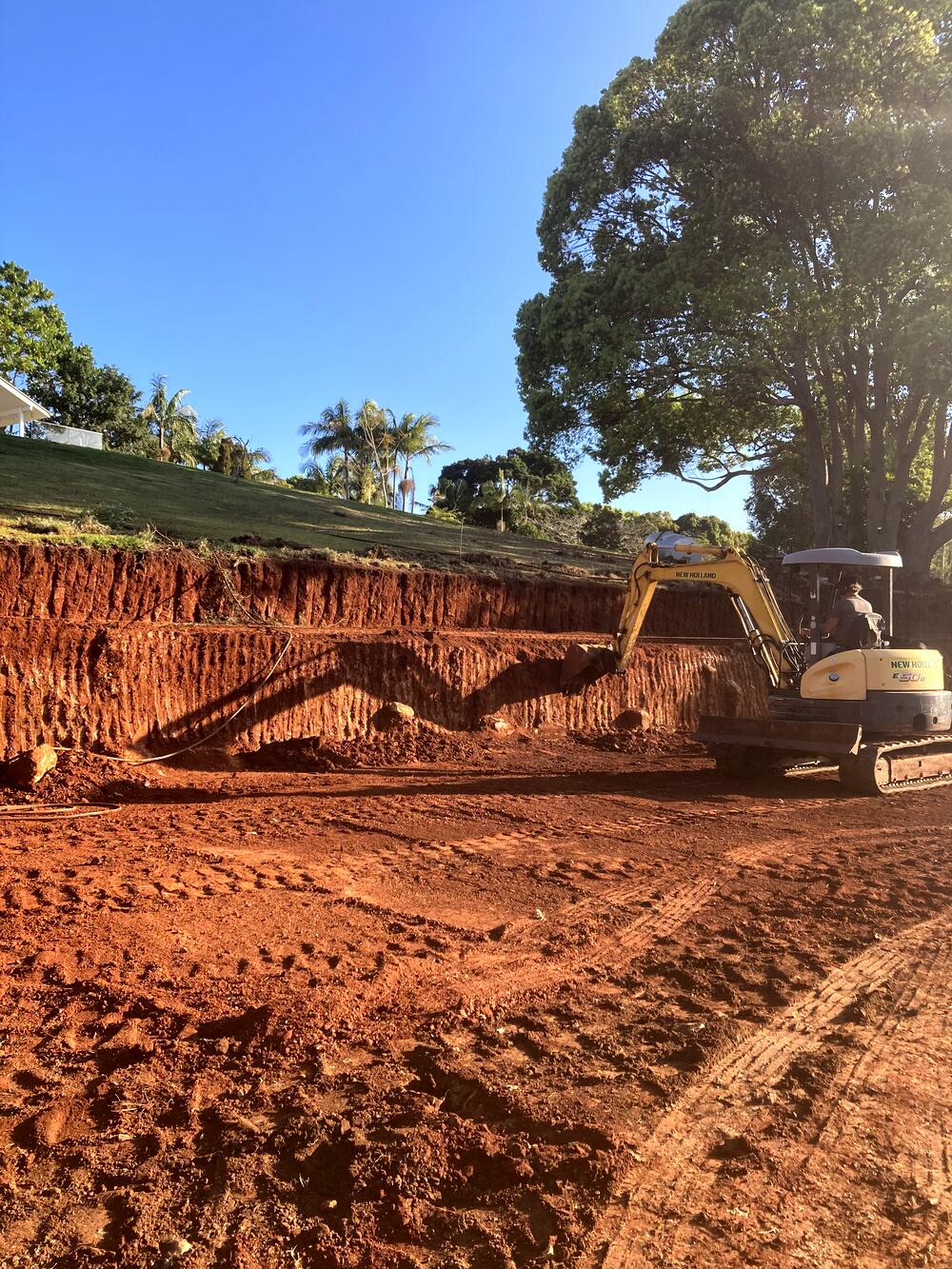 A large benched cut in red soil with the excavator working the batter