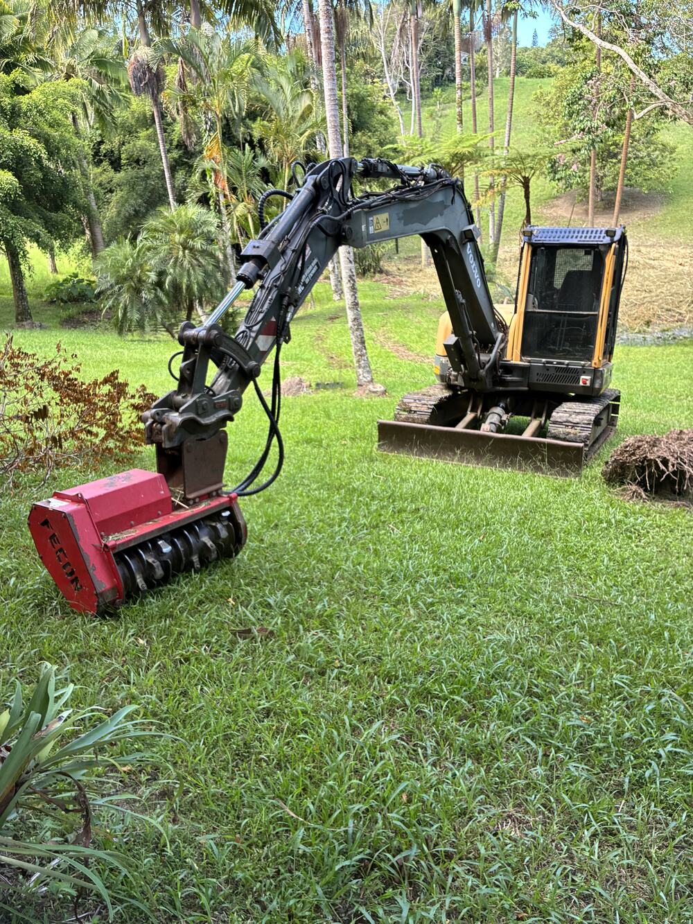 Excavator fitted with the mulcher attachment on a grassed hillside block